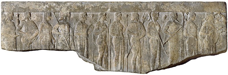 Фрагмент эллинистического рельефа из Художественного музея Уолтерса: Гестия (скипетр), Гермес (крылатая шапка и посох), Афродита (в покрывале), Арес (шлем и копье), Деметра (скипетр и сноп пшеницы), Гефест (посох), Гера (скипетр), Посейдон (трезубец), Афина (сова и шлем), Зевс (молния и посох), Артемида (лук и колчан) и Аполлон (лира)